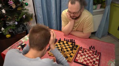 Baba ve oğul satranç oynuyor. Genç çocuk babasıyla oynuyor. Evde ailecek vakit geçiririz..