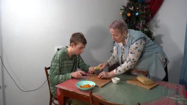 Oğlan ve büyükanne hamuru kesip turta yiyorlar. Evde yemek pişirmek. Noel için yemek pişiriyorum. Yemek hazır.