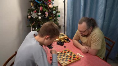 Ergen, babasıyla dama oynuyor. Satranç tahtası. Oğlan ve babası evde masa oyunu oynuyorlar. Noel zamanı