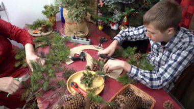 Yapıştırıcı ladin dalları. Büyükannem ve torunum birlikte Noel çelengi yapıyorlar. Yaşlı kadın ve genç çocuk dekore ediyor. Aile Zirvesi Aralık