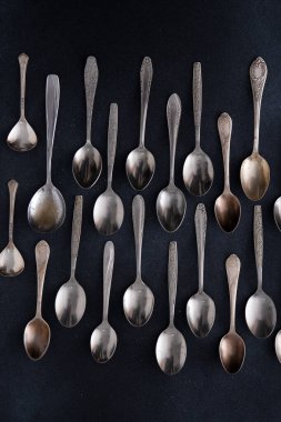 Farklı kaşıklar. Siyah arka planda gümüş çatal bıçak seti. Servis kaşığı masada.
