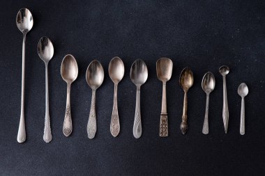Farklı çay kaşıkları. Siyah arka planda gümüş çatal bıçak seti. Masanın üstünde kaşık