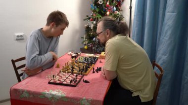 Baba ve oğul satranç oynuyor. Genç çocuk babasıyla oynuyor. Evde ailecek vakit geçiriyoruz. Evde vakit geçirmek.