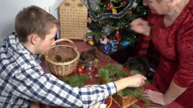 Büyükannem ve torunum Noel süslerini dallardan, kozalaklardan ve mumlardan yapıyorlar. Yaşlı kadın ve genç çocuk sepetlerini kendi elleriyle dekore ederler. DIY Kış Gemisi