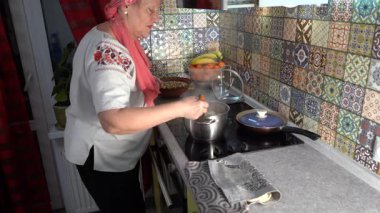 Yaşlı kadın yemek pişiriyor. Büyükannem tencerede hamur köftesi pişirir. Sobanın üzerinde ahşap bir spatulayla karıştır. Evde yemek pişirmek..