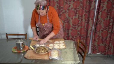 Yaşlı bir kadın etli börek yapar. Ev yapımı hamur. Büyükannem evde yemek pişiriyor. Eller aşçı.