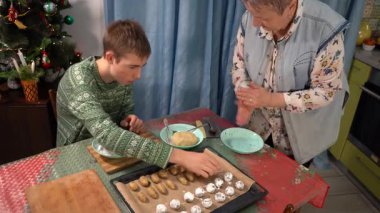 Genç çocuk büyükannesiyle Noel kurabiyesi yapıyor. Çikolatalı mermer kurabiyeler pudra şekerinde yuvarlanıyor. Tatlı tatlı tatlı. Evde yemek pişirmek. Aile