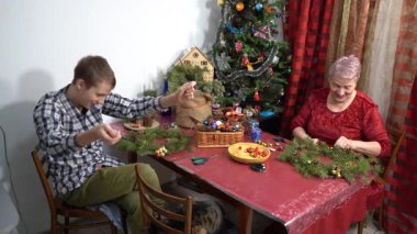 Büyükannem ve torunum birlikte Noel çelengi yapıyorlar. Yaşlı kadın dekore ediyor. Çocuk kediyle oynuyor. Evde aile eğlencesi. Zanaat
