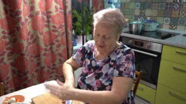 Yaşlı bir kadın mutfakta yemek hazırlıyor. Sarımsaklı sebze ve meyve salatası kesiyor..