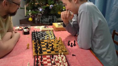 Baba ve oğul aynı anda üç tahtada satranç oynarlar. Genç çocuk babasıyla oynuyor. Evde ailecek vakit geçiririz..