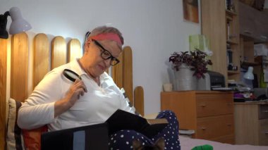 Gözlük takan ve elinde büyüteç tutan bir büyükanne. Yaşlı bir kadın yatakta oturmuş posta pullarından oluşan bir albüme bakıyor. Büyükannem ve hobisi evde. Kitap