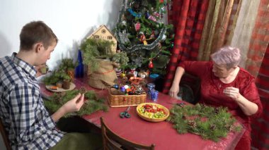 Büyükannem ve torunum birlikte Noel çelengi yapıyorlar. Yaşlı kadın ve genç çocuk evde dekore ediyorlar. Aile eğlencesi. Zanaat