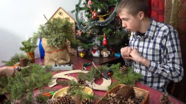 Çocuk Noel çelengi yapıyor. Gençler ladin dallarını süsler. Evde sıcak yapıştırıcı var. Kış aktiviteleri.