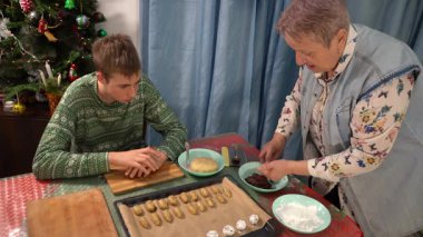 Çatlaklı çikolatalı mermer kurabiyeler yap. Oğlan ve büyükanne hamur işi pişiriyor. Ergen ve yaşlı kadın yemek pişirir. Pişirme tepsisindeki gübre. Tablo