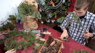 Genç çocuk budama makası ile ladin dalları kesiyor. Evde Noel çelengi yap. Kış tatili teknesi. Tablo üstü görünümü