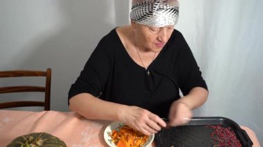 Yaşlı bir kadın tohumları taze bir balkabağından ayırıyor. Bir büyükanne mutfaktaki masada yemek hazırlar. Ev yemeği.