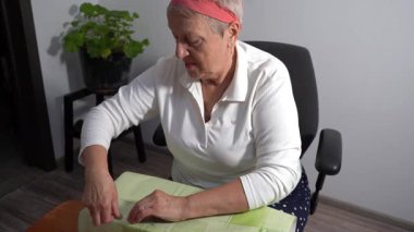 Yaşlı bir kadın hediyesini yeşil kağıda sarar. Bir büyükanne evde bir kutu toplar. Eller sarılıyor..