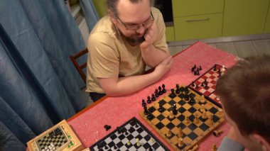 Baba ve oğul aynı anda üç tahtada satranç oynarlar. Genç çocuk babasıyla oynuyor. Evde ailecek vakit geçiririz..