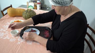 Yaşlı bir kadın kurutulmuş böğürtlen hasadını sınıflandırıyor. Bir büyükanne mutfaktaki masada yemek hazırlar. Ev yemeği. Çalışan eller