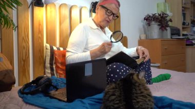 Büyükannem büyüteçle okur. Yaşlı bir kadın yatakta oturmuş posta pullarından oluşan bir albüme bakıyor. Büyükanne ve hobisi evde.