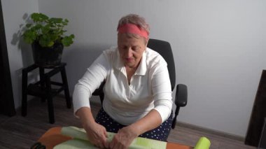 Yaşlı bir kadın hediyesini yeşil kağıda sarar. Bir büyükanne evde bir kutu toplar. Eller çalışıyor.