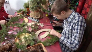 Çocuk dalları ve konileri sıcak yapıştırıcıyla yapıştırdı. Noel çelengi yap. Genç çocuk el sanatları süsledi. DIY Evinde