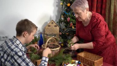 Büyükannem ve torunum birlikte Noel süsü yapıyorlar. Yaşlı bir kadın ve genç bir oğlan. Çam dalları. Kış ev yapımı. Aile numarası.
