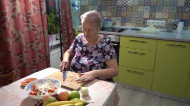 Sarımsak kes. Yaşlı bir kadın mutfakta yemek pişiriyor. O, sebze ve meyve dolu bir salata kasesi kesiyor..