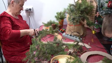Yapıştırıcı ladin dalları. Büyükannem Noel çelengi dekoru yapıyor. Yaşlı bir kadın ev yapımı süsleme yapıyor. Aile kış geleneği