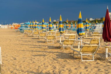 Kumsalda, Şemsiyeli ve Güverte Sandalyeli. Yaz tatili. Boş sahil şeridi şezlongu. Sarı mavi şemsiye güneş banyosu