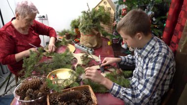 Tutkal çam dalları. Büyükannem ve torunum birlikte Noel çelengi yapıyorlar. Yaşlı kadın ve genç çocuk dekore ediyor. Aile aktiviteleri. Zanaat