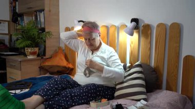 Yaşlı bir kadın mücevherlerini deniyor. Gri saçlı bir büyükanne zincirine kolye takar. Evde yatakta otur. Boynunda boncuklar var. Mücevher kutusu..