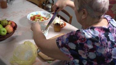 Yaşlı bir kadın mutfakta balık yemeği hazırlıyor. Tahtayı kesiyor. Ringa balığı kasesi