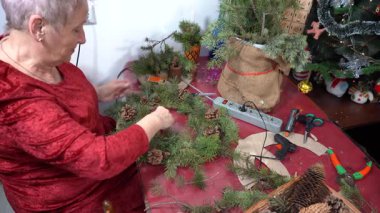 Büyükannem Noel çelengi, dal ve koni yapıyor. Yaşlı kadın ladin süsler. Kış etkinlikleri. Zanaat