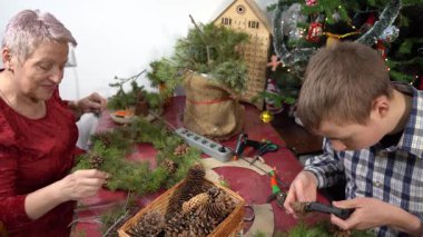 Büyükannem ve torunum birlikte Noel çelengi yapıyorlar. Yaşlı kadın ve genç çocuk çam dalları süsler. Yapıştırıcı, Aile Kışlık Sanatı