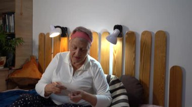 Yaşlı bir kadın yatakta oturur ve altın mücevherlerine bakar. Büyükannem ve onun hazine boncukları.