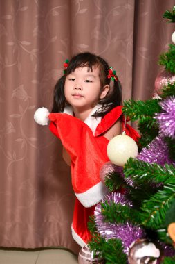 Noel festivali ve yeni yıl kutlaması için Noel Baba kostümü giymiş küçük bir Asyalı kızın portresi.