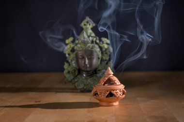 Tütsü ocağında yanan tütsü. Masanın üzerinde koyu arkaplanı olan bir Buda heykeli var. Din kavramı