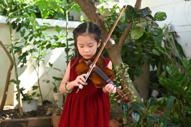 Bahçede keman çalan tatlı Asyalı küçük kız.
