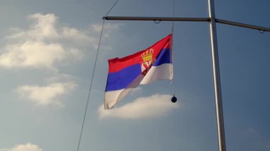 Sırbistan bayrağı gökyüzü ve bulutların karşısında bayrak direği sallıyor