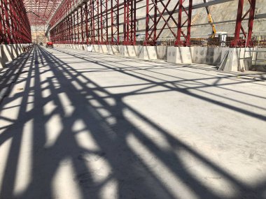 Kirişler, kirişler ve metal sütunlar beton zemine gölge düşürüyor. Destek yapıları. Endüstriyel metal yapı iskeleti. Düşük açı görünümü