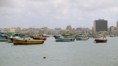 İskenderiye limanına demir atmış balıkçı tekneleri. Yatlar ve balıkçı tekneleri limandaki deniz dalgalarında sallanıyor. Arkadaki Alexandria Corniche