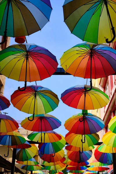 Lots of rainbow-colored umbrellas hanging above street. Decoration of streets made of umbrellas