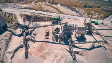 Ön yükleyici çöp kamyonunu ezilmiş taşla dolduruyor. Taş kıran bitkilerin hava manzarası. Taşıyıcılar, silolar ve açık kireçtaşı madeninin diğer yapıları. İnşaat malzemeleri üretimi