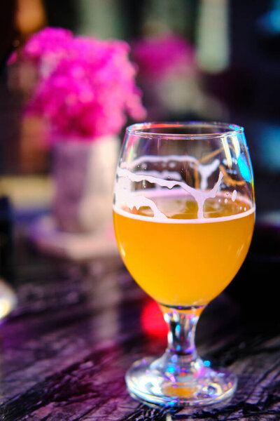 Glass of beer stands on a table opposite bright pink flowers at background