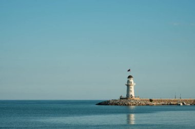 Rıhtımdaki deniz feneri. Deniz feneri, sakin deniz ve berrak gökyüzü olan minimalist deniz manzarası