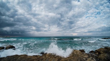Akan deniz dalgaları kayalık sahil şeridine çarpıyor. Deniz dalgaları kayalara çarpıyor. Bulutlar ve akan denizle ultra geniş açı manzarası