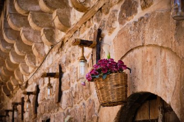 Hasır sepette çiçekler ve taş duvarda asılı lambalar. Sokak dekorasyonu. Çiçeklerle dolu bir sepet.