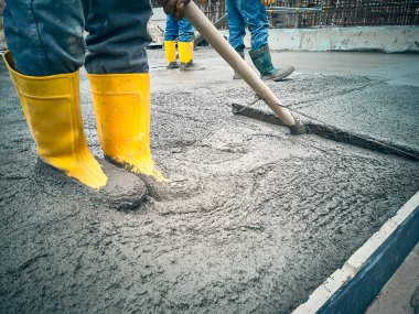 İnşaat işçisi havan topunu düzleştirmek için boğa kullanıyor. İnşaat alanında beton işi var. Mala kullanarak döküm çalışması. 