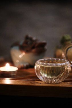Ahşap çay tepsisine konmuş çay dolu şeffaf cam bardak. Küçük yanan çay mumu huzurlu ve rahat bir atmosfer yaratıyor. Rahatlık ve sıcaklıkla yapılan çay seremonisi estetiği. 